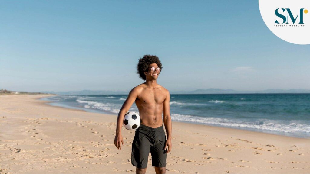 Smiling African American male standing with ball on seashore